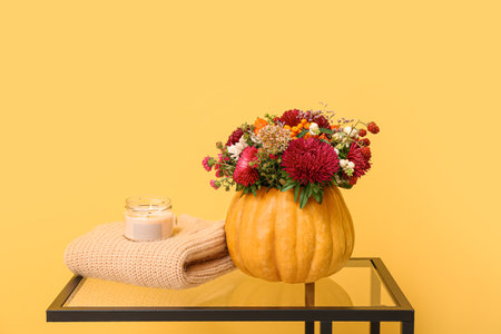 Beautiful autumn bouquet in pumpkin and burning candle on table against yellow backgroundの写真素材