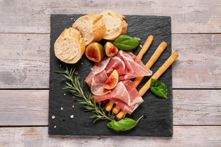 Board with slices of tasty prosciutto, basil, bread, Italian Grissini and figs on gray wooden backgroundの写真素材