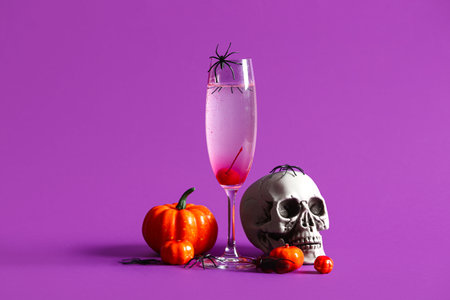 Glass of delicious cocktail, skull and pumpkins for Halloween celebration on purple backgroundの写真素材