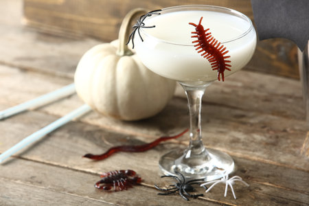 Glass of delicious white cocktail and candy bugs for Halloween celebration on wooden background, closeupの写真素材