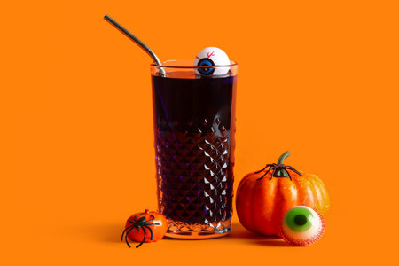 Glass of delicious cocktail, eyes and pumpkins for Halloween celebration on orange backgroundの写真素材