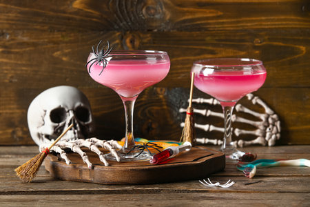 Glasses of delicious pink cocktail and skeleton hands for Halloween celebration on wooden backgroundの写真素材