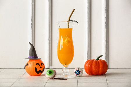 Glass of delicious orange cocktail, pumpkin and eyes for Halloween celebration on light backgroundの写真素材