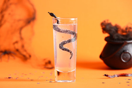 Shot of delicious cocktail and snake for Halloween celebration on orange background, closeup