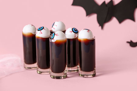 Shots of delicious cocktail and eyes for Halloween celebration on pink backgroundの写真素材