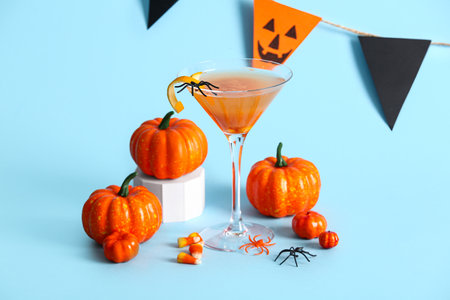 Glass of delicious orange cocktail, candy corns and pumpkins for Halloween celebration on blue backgroundの写真素材