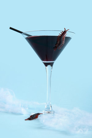 Glass of delicious cocktail and candy bugs for Halloween celebration on blue backgroundの写真素材
