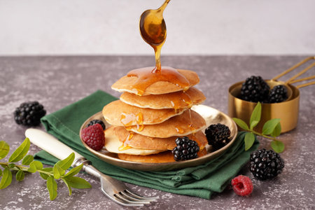 Pouring of maple syrup onto tasty pancakes with berries on table