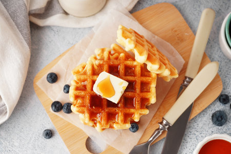 Wooden board of tasty waffles with blueberries and maple syrup on white backgroundの写真素材