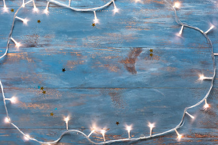 Frame made of glowing Christmas lights on blue wooden backgroundの写真素材
