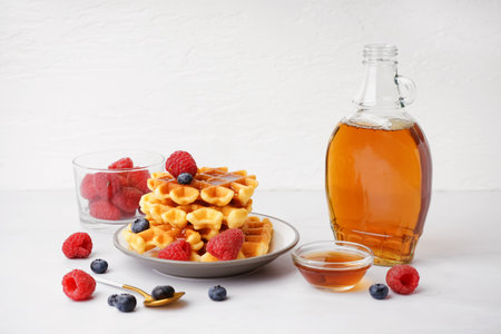 Plate of tasty waffles with berries and maple syrup on white backgroundの写真素材