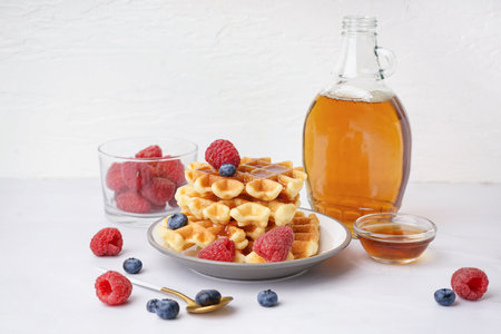 Plate of tasty waffles with berries and maple syrup on white backgroundの写真素材