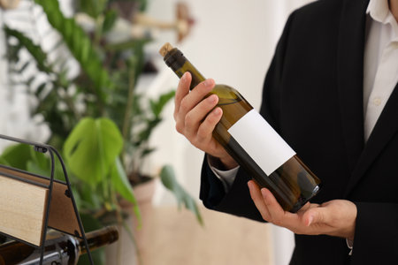 Young sommelier with bottle of wine in kitchen, closeupの写真素材