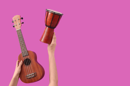 Female hands holding ukulele and drum on pink backgroundの写真素材