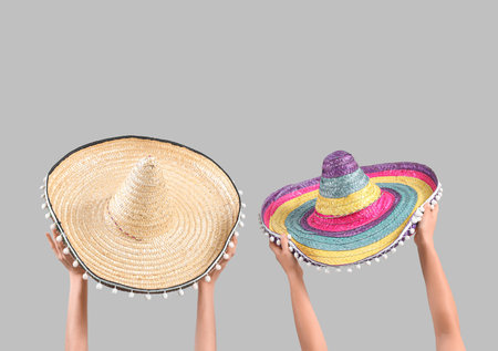Female hands holding sombreros on gray backgroundの写真素材