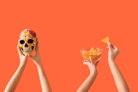 Female hands holding nachos and painted human skull for Mexico's Day of the Dead (El Dia de Muertos)...