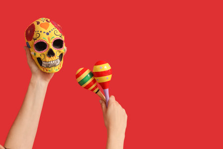 Female hands holding painted human skull for Mexico's Day of the Dead (El Dia de Muertos) and maracas on red backgroundの写真素材