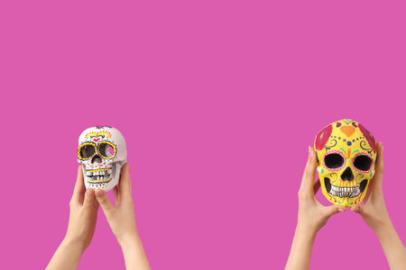 Female hands holding painted human skulls for Mexico's Day of the Dead (El Dia de Muertos) on pink...