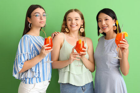 Beautiful young women with glasses of tasty spritz cocktail on green backgroundの写真素材