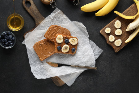 Baking paper of toasts with peanut butter, fresh fruits and honey on black backgroundの写真素材