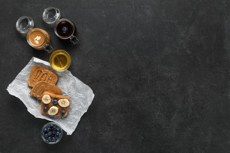 Baking paper of toasts with peanut butter, fresh fruits and honey on black backgroundの写真素材