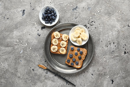 Plate of toasts with peanut butter, blueberries and banana on gray background