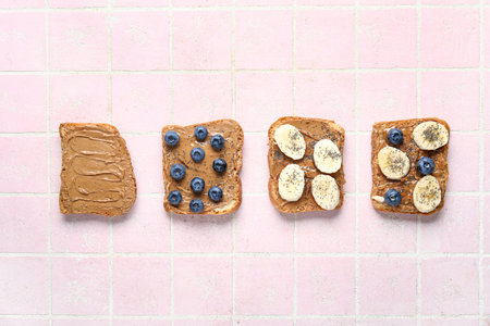 Toasts with peanut butter, fresh fruits and poppy seeds on pink tile backgroundの写真素材
