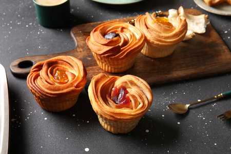 Wooden board of tasty cruffins with jam on black background