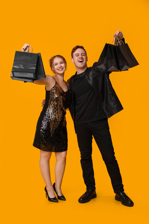 Young couple with shopping bags on yellow background. Black Friday saleの写真素材