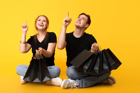 Young couple with shopping bags pointing at something on yellow background. Black Friday sale