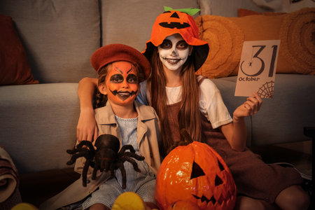 Little girls dressed for Halloween with toy spider and card at home in eveningの写真素材