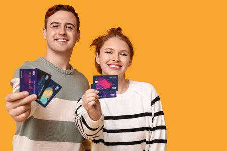 Young couple with credit cards on yellow backgroundの写真素材