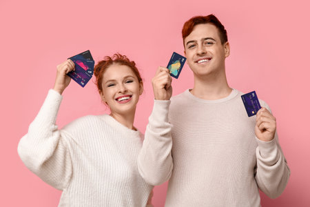 Young couple with credit cards on pink backgroundの写真素材