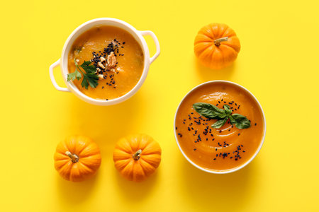 Bowl and pot of delicious pumpkin cream soup on yellow backgroundの写真素材