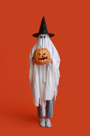 Young woman in Halloween costume of ghost with witch hat and pumpkin on color backgroundの写真素材