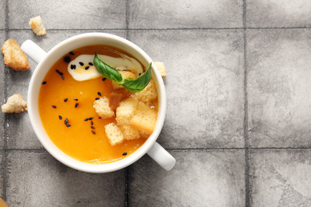 Pot of delicious pumpkin cream soup with croutons and basil on gray tile backgroundの写真素材