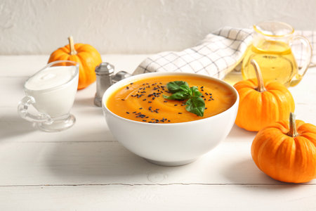 Bowl of delicious pumpkin cream soup with seeds and basil on white wooden tableの写真素材