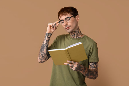 Young tattooed man reading book on brown backgroundの写真素材