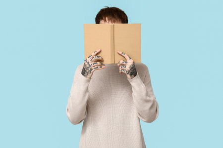 Young tattooed man with book on blue backgroundの写真素材