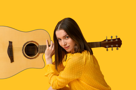 Pretty young woman with acoustic guitar on yellow backgroundの写真素材