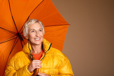 Beautiful mature woman with umbrella on brown backgroundの写真素材