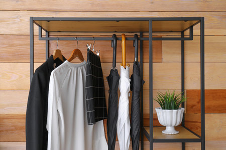 Rack with clothes, umbrellas and plant near wooden wall, closeupの写真素材