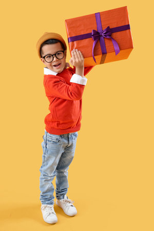 Little Asian boy with gift on yellow backgroundの写真素材
