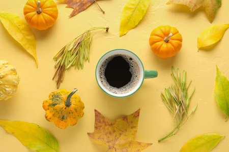 Composition with cup of aromatic coffee, pumpkins and fallen leaves on color backgroundの写真素材