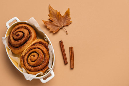 Baking dish of tasty cinnamon rolls and autumn leaf on brown backgroundの写真素材
