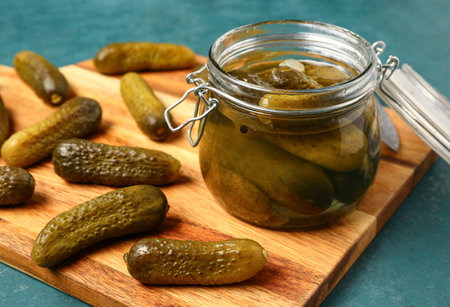 Jar and wooden board with tasty pickled cucumbers on color backgroundの写真素材