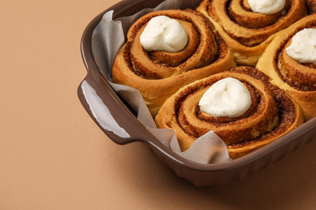 Baking dish of tasty cinnamon rolls with cream on brown backgroundの写真素材