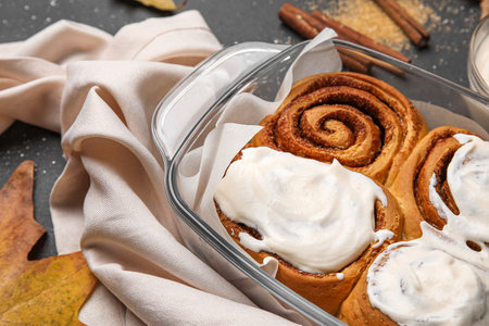 Baking dish of tasty cinnamon rolls with cream on black backgroundの写真素材