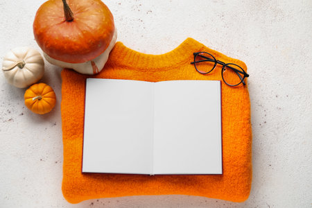 Composition with warm sweater, book, eyeglasses and pumpkins on light backgroundの写真素材