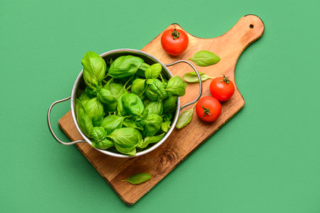Wooden board with cooking pot of fresh green basil and tomatoes on color backgroundの写真素材